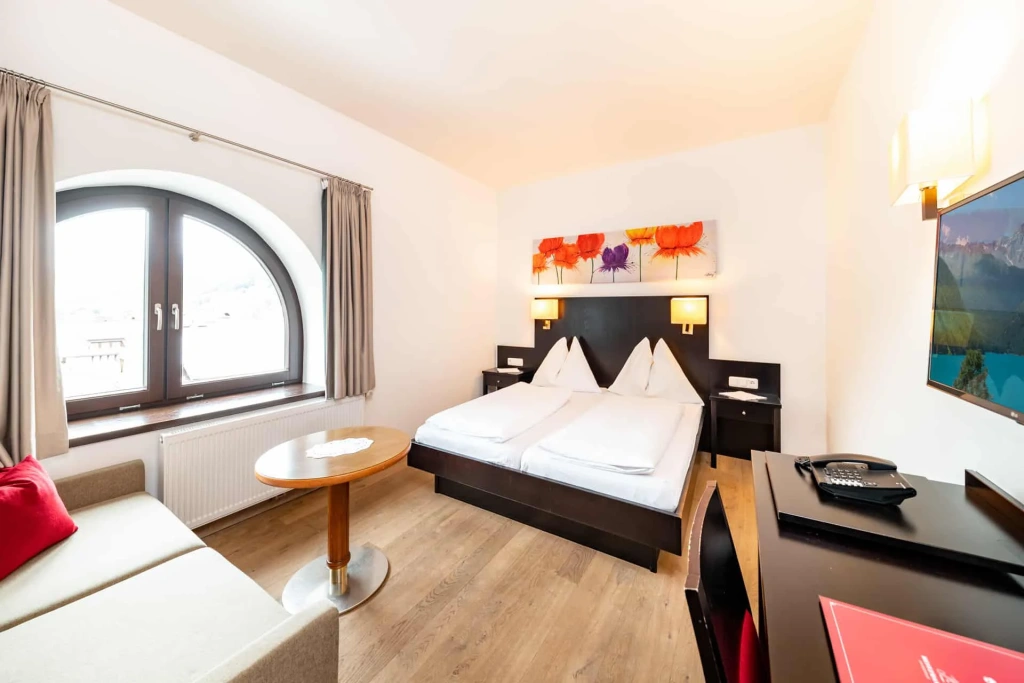 Bright hotel room with a double bed, sofa, desk, and large window with a view