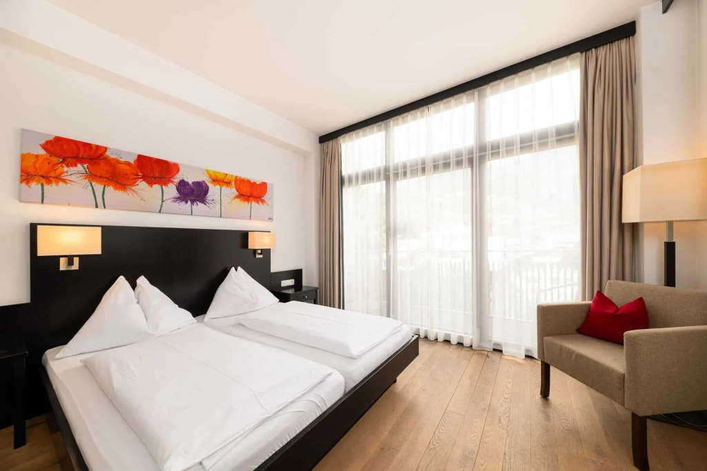 Modern hotel room with double bed, armchair, wooden floor and large window with a view
