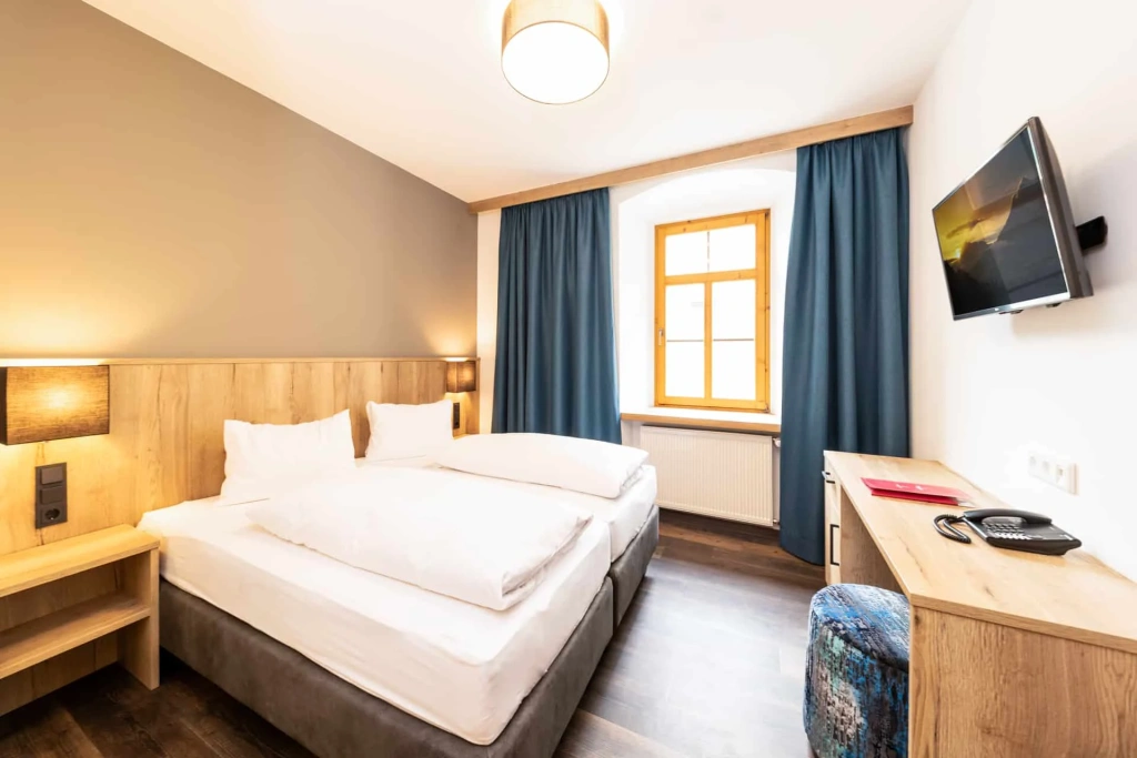 Modern hotel room with double bed, desk, TV, and window with blue curtains