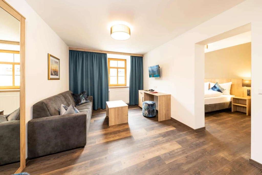 Modern hotel room with sofa, desk, TV, and separate bedroom