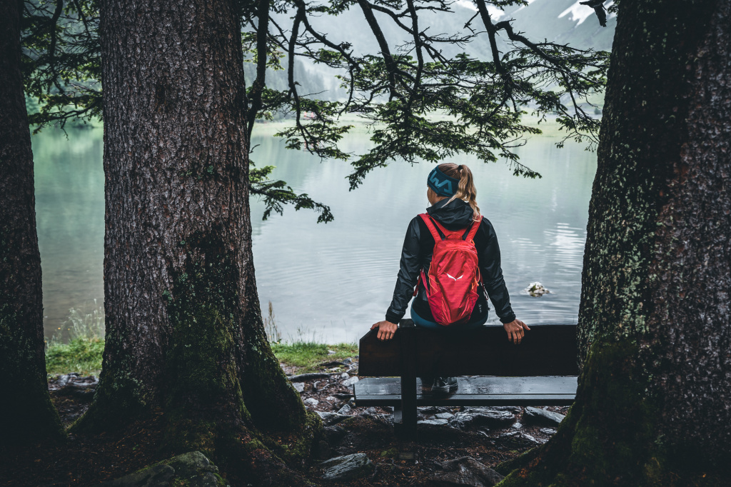 Hiker with a red rucksack sitting on a bench by the lake